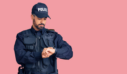 Young hispanic man wearing police uniform checking the time on wrist watch, relaxed and confident