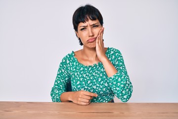 Beautiful brunettte woman wearing casual clothes sitting on the table touching mouth with hand with painful expression because of toothache or dental illness on teeth. dentist