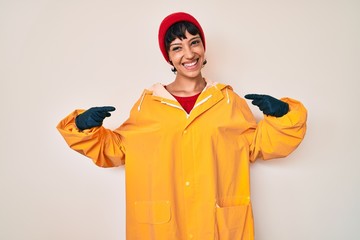 Beautiful brunettte woman wearing yellow raincoat looking confident with smile on face, pointing oneself with fingers proud and happy.