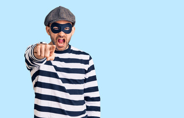 Young handsome man wearing burglar mask pointing displeased and frustrated to the camera, angry and furious with you