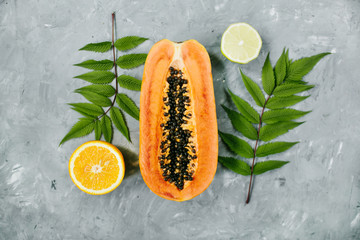 Summer tropical composition. Green leaves and tropical fruits (Papaya, orange, lemon) on gray background. Summer concept. Flat lay, top view.Tropical travel, exotic fruit. Vegan and vegetarian concept