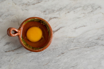 yema y clara de huevo dentro de un recipiente de barro, sobre una barra de mármol gris.