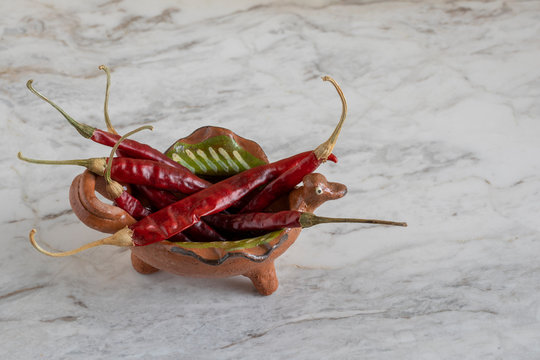 chiles de &aacute;rbol o chiles secos rojos,  en un vasija de barro, sobre una barra de m&aacute;rmol gris.