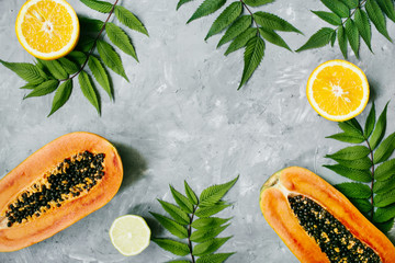 Summer tropical composition. Green leaves and tropical fruits (Papaya, orange, lemon) on gray background. Summer concept. Flat lay, top view, copy space