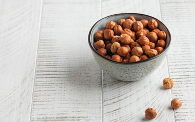 A handful of hazelnuts in a grey bowl on a white wooden background. Healthy snacks. Nuts. Copy space.