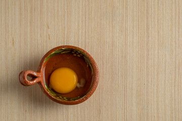 Vasija de barro con una yema con clara, sobre una superficie de madera. Con espacio para texto en la parte lateral.