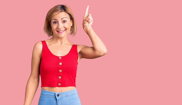 Young blonde woman wearing casual clothes pointing finger up with successful idea. exited and happy. number one.