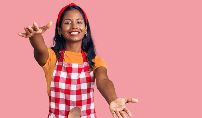 Young indian girl wearing professional baker apron looking at the camera smiling with open arms for...