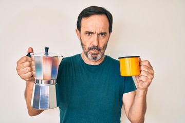 Middle age hispanic man holding italian coffee maker skeptic and nervous, frowning upset because of problem. negative person.