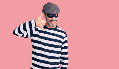 Middle age handsome man wearing burglar mask smiling doing phone gesture with hand and fingers like talking on the telephone. communicating concepts.