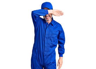 Middle age handsome man wearing mechanic uniform covering eyes with arm smiling cheerful and funny. blind concept.