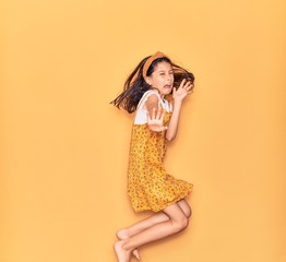 Adorable hispanic child girl wearing casual dress and diadem smiling happy. Jumping with smile on face over isolated yellow background