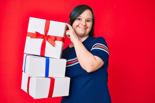 Brunette woman with down syndrome holding gifts smiling with a happy and cool smile on face. showing teeth.