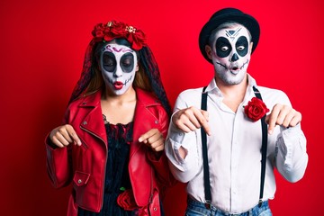 Obraz premium Couple wearing day of the dead costume over red pointing down with fingers showing advertisement, surprised face and open mouth