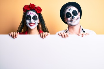 Couple wearing day of the dead costume holding blank empty banner looking positive and happy standing and smiling with a confident smile showing teeth
