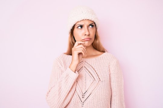 Young brunette woman wearing winter hat and sweater thinking concentrated about doubt with finger on chin and looking up wondering
