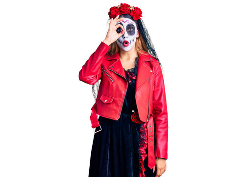 Woman wearing day of the dead costume over background doing ok gesture shocked with surprised face, eye looking through fingers. unbelieving expression.