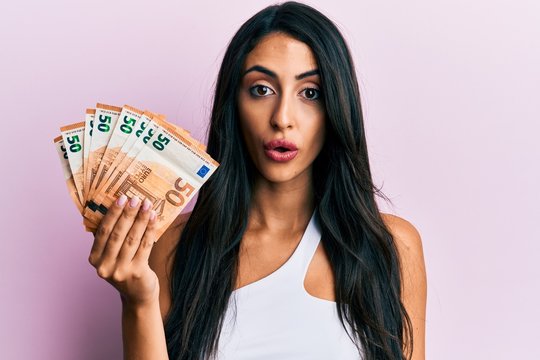 Beautiful hispanic woman holding 50 euro banknotes scared and amazed with open mouth for surprise, disbelief face