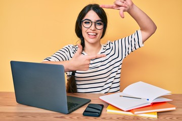 Brunette teenager girl working at the office with laptop smiling making frame with hands and fingers with happy face. creativity and photography concept.