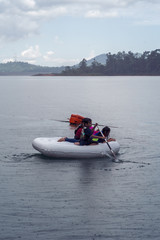 Fototapeta na wymiar Family wearing life jackets paddling on an inflatable boat in Kenyir Lake, Malaysia.