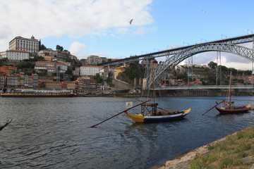 Fototapeta na wymiar Dom Luis I bridge and traditional boats with wine barrels on Rio Douro river in Porto, Portugal