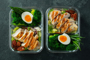 Healthy meal prep containers with green beans, chicken breast and broccoli. A set of food for keto diet in lunchbox on a dark concrete background. Top view
