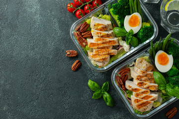 Healthy meal prep containers with green beans, chicken breast and broccoli. A set of food for keto diet in lunchbox on a dark concrete background. Top view with copy space