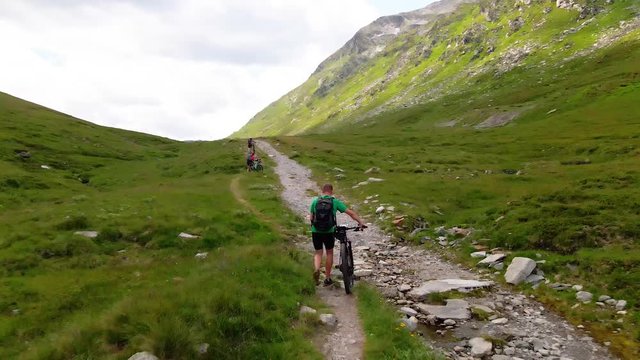 Three mountainbikers pushing up their bikes on a steep track in the Alps.