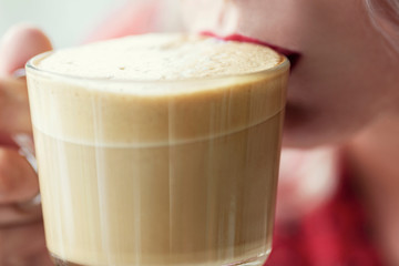 Cup of coffee with foam near woman lips. Close-up.