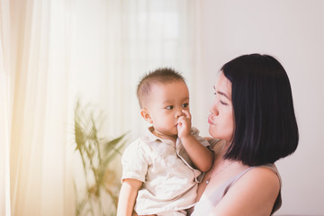 Adorable asian baby boy sucking thumb with mom carrying in bedroom,Happy new born kid