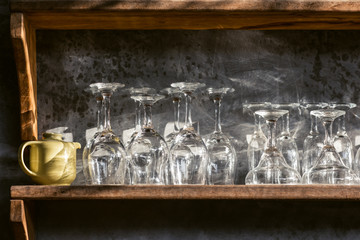 Set of different champagne, wine, martini empty clean glasses on bar restaurant wooden shelf. Gray concrete wall, loft interior design. Shining sun light.