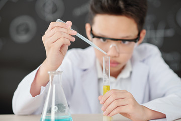 Vietnamese schoolboy adding drop of reagent in test-tube with yellow liquid