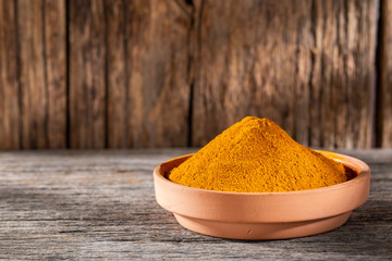 Turmeric powder in bowl on wooden background