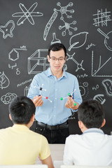 Smiling Asian science teacher showing plastic molecular models to curious school stundets
