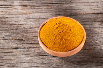 Turmeric powder in bowl on wooden background