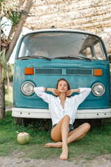 Woman is sitting near blue vintage van car. Hipster tourist girl  in her camper van near the beach...