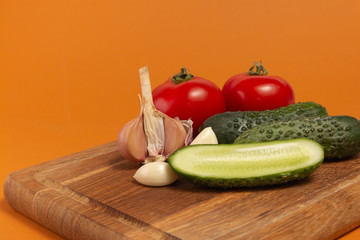 Sliced cucumber, tomatoes and garlic on wooden cutting board. Tomatoes with green ponytails. Healthy food. Copy space. High quality close-up photo