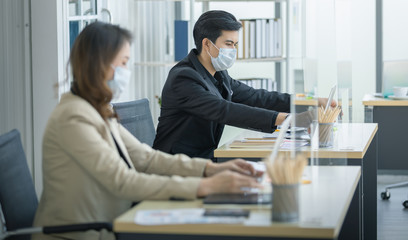 Business office working together at new normal social distance with table shield partition reduce infection of coronavirus covid-19 pandemic. Social and business distancing new normal lifestyle.