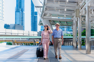 tourist older woman and man wearing casual dress , hand holding baggage for travel walking and talking passed the public sky walk bridge.