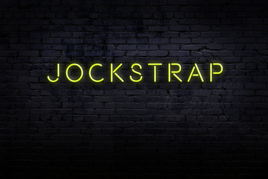 Neon sign. Word jockstrap against brick wall. Night view