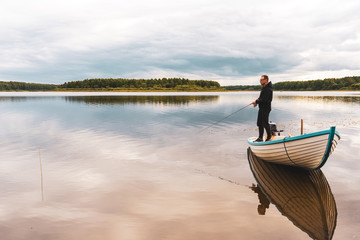 Fototapeta na wymiar An elderly man is fishing from a boat near the shore on the lake