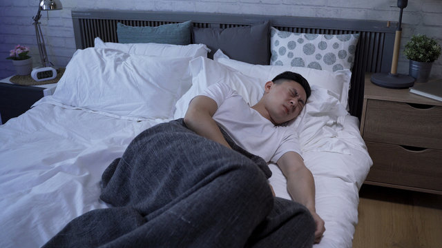asian male tossing and turning on bed is having a disturbed sleep. closeup japanese guy waking up from a nightmare is sitting and mopping the sweat from his brow.