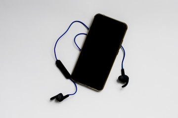 Black mobile phone with headphones and blank screen flat lay minimalism concept Earphones with mobile phone