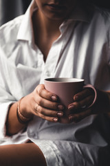 Woman in a white t-shirt holds morning coffee in a pink ceramic cup. Manicure. Front view