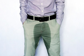 Problems with bladder. The concept of men's health. Young man in light trousers with wet stain from...