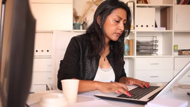 Portrait of troubled Hispanic female manager looking worriedly at laptop screen in office. High quality FullHD footage
