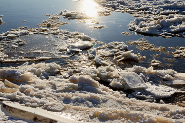 Ice drift on a river with blue high water and big water, white snow broken ice full of hummocks in it and sun reflection in sunny spring day.
