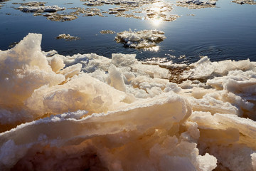 Ice drift on a river with blue high water and big water, white snow broken ice full of hummocks in it and sun reflection in sunny spring day.