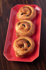 puff pastry cinnamon rolls with custard and raisins dark in a red plate wooden background.Top view, space.