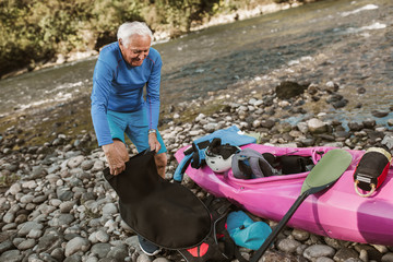 Senior man preparing for kayak tour on a mountain river.